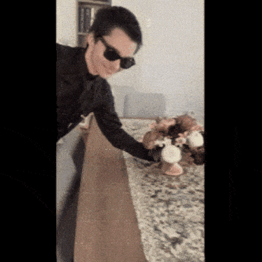 a man wearing sunglasses is reaching for a vase of flowers