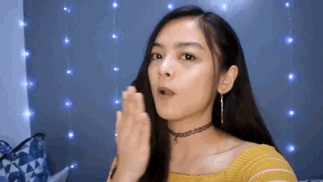 a woman wearing a yellow sweater and a choker looks surprised