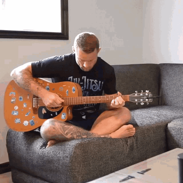a man sitting on a couch playing a guitar with a jiu-jitsu shirt on