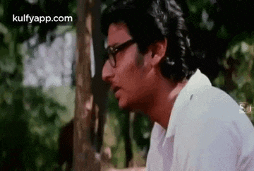 a man wearing glasses and a white shirt is sitting in a forest .