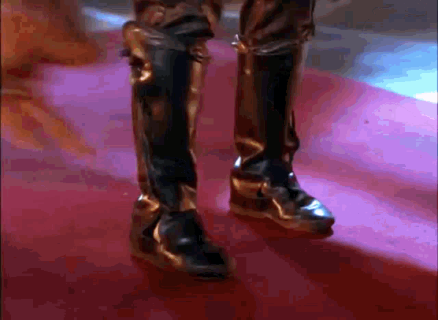a pair of black and gold boots on a pink carpet