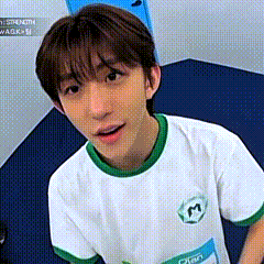 a young man wearing a white shirt with a green collar and sleeves is sitting on a blue mat .