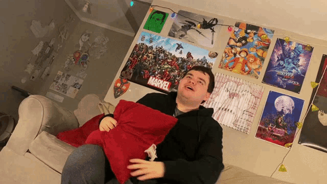 a man is sitting on a couch with a marvel poster on the wall behind him