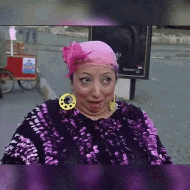 a woman wearing a pink head scarf and earrings is making a face