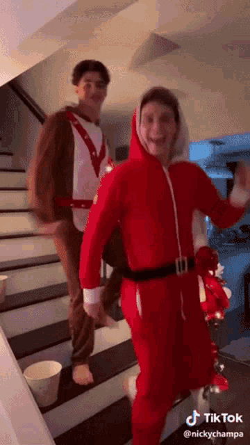 a man in a santa suit is walking down stairs next to another man in a reindeer suit