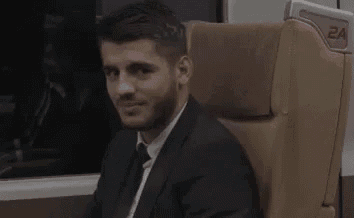 a man in a suit and tie is sitting in a chair on a train and smiling .