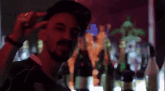 a man with a beard wearing a hat stands in front of a bar full of bottles