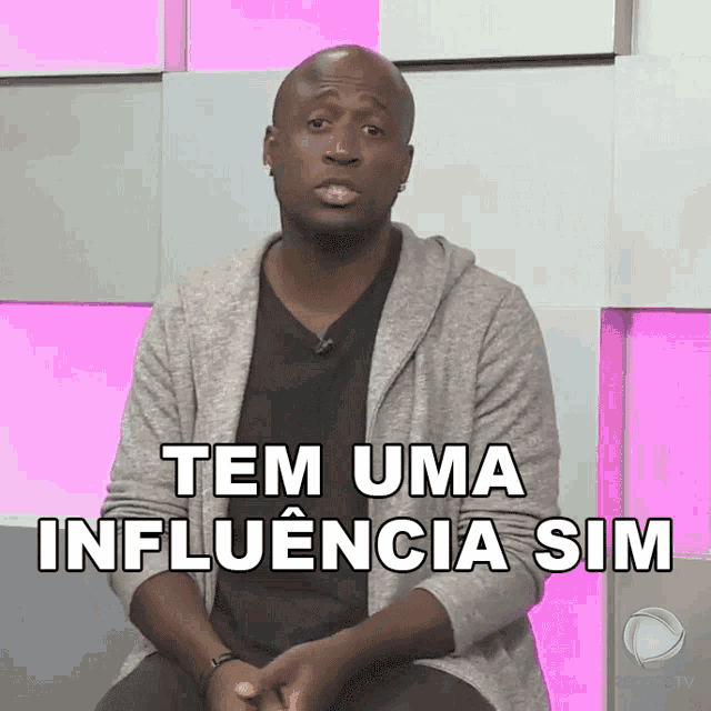 a man sitting in front of a pink wall with the words tem uma influencia sim