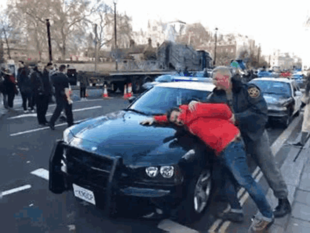 a man in a red jacket is being arrested by a police officer .