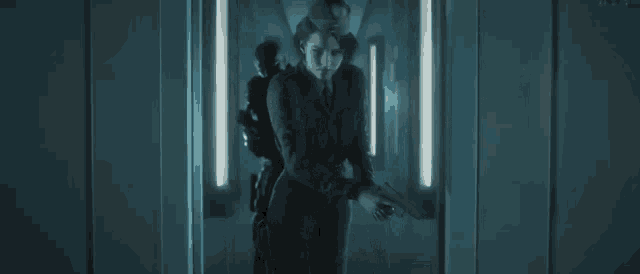 a man in a suit and tie is standing in a dark hallway holding a gun .