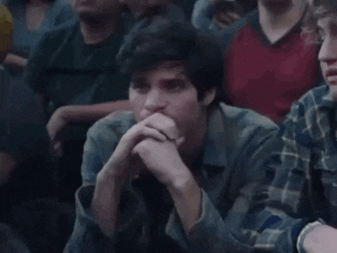 a man is sitting in a crowd of people with his hands on his chin and looking at something .