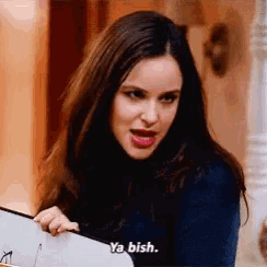 a woman is making a funny face while holding a book and saying ya mish .