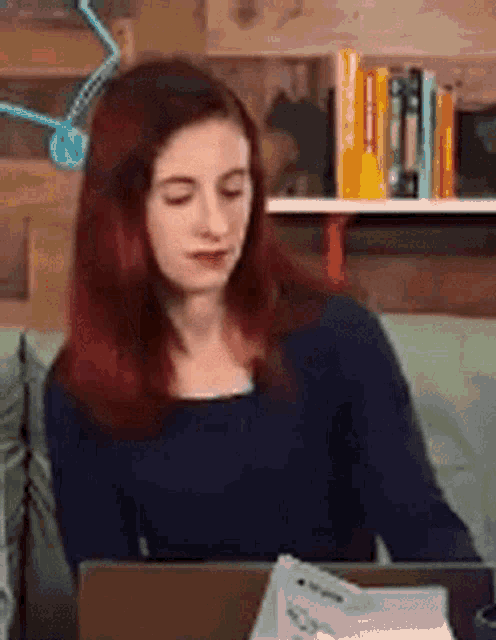 a woman with red hair is sitting at a desk with a laptop and papers