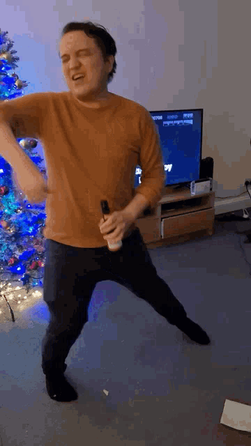 a man is dancing in front of a christmas tree while holding a wii controller