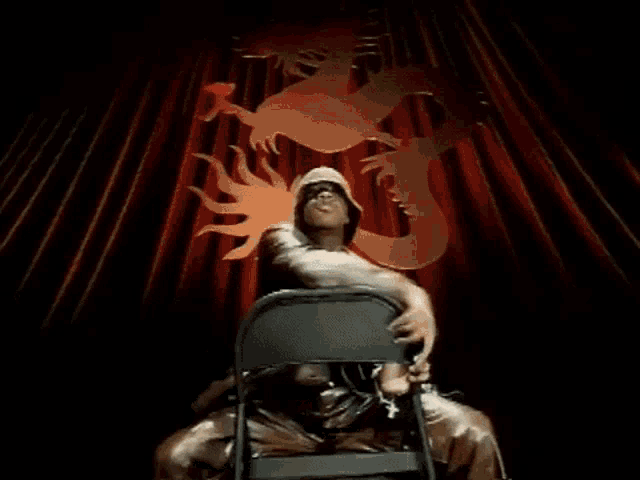 a man is sitting in a chair in front of a red curtain .