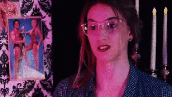 a woman with glasses stands in front of a picture of a man and a woman