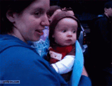 a woman is holding a baby in a blue sling with a gifbin.com logo in the corner