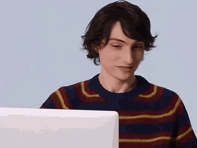 a young man in a striped sweater is looking at a laptop .