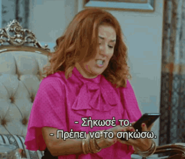 a woman in a pink shirt is looking at a cell phone with greek writing on it