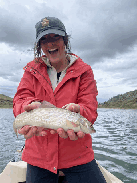 a woman in a red jacket is holding a fish and smiling