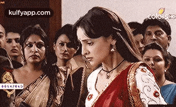 a group of people are standing around a woman in a red saree .