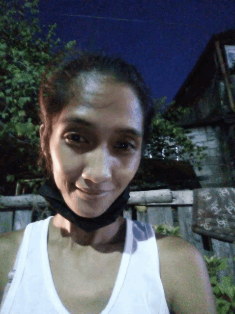 a woman wearing a black mask and a white tank top smiles