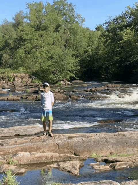 a man in a white shirt stands on a rock near a river