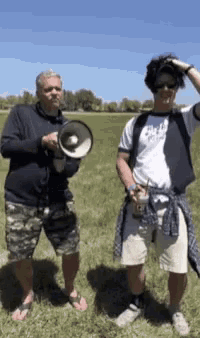 a man holding a megaphone next to another man in a field