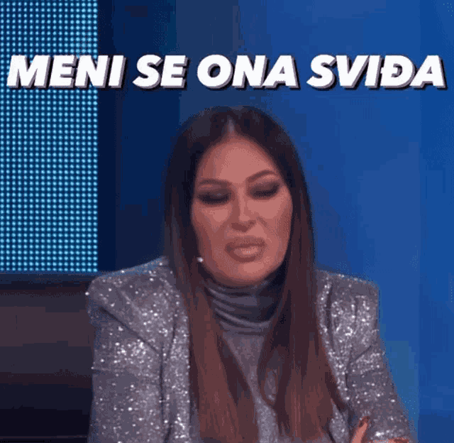 a woman is sitting in front of a blue screen with the words `` meni se ona svida '' written on it .