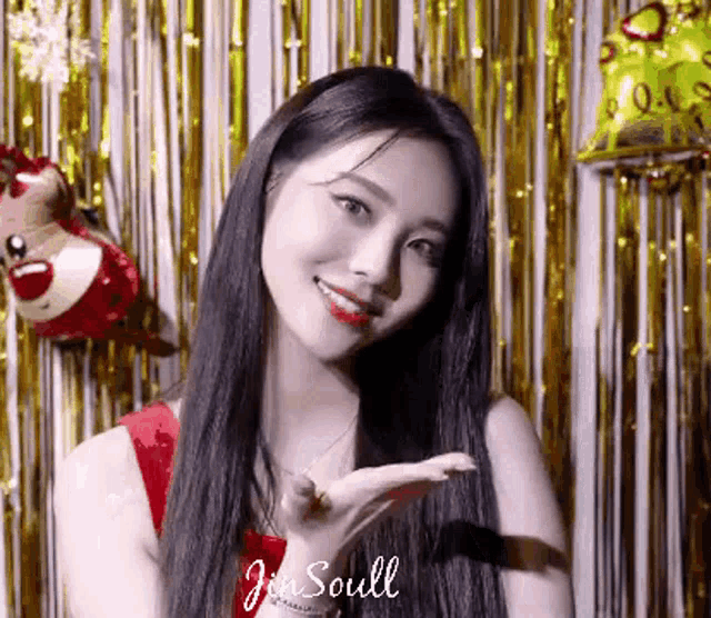 a woman with long black hair is standing in front of a gold curtain and balloons and smiling .