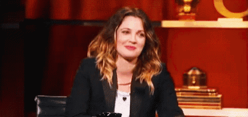 a woman in a tuxedo is sitting at a table in front of a red curtain and smiling .