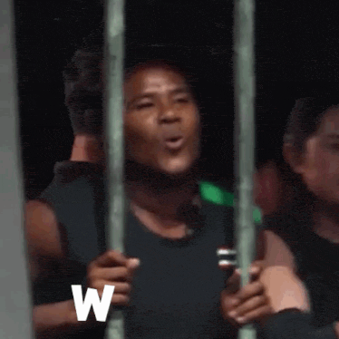a man is standing behind bars in a prison cell talking on a cell phone .