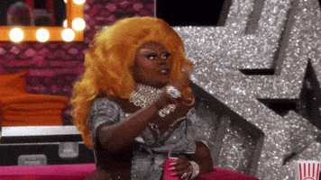 a drag queen is sitting at a table with a can of soda