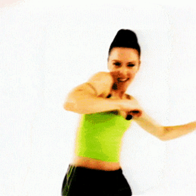 a woman in a green tank top and black shorts is pointing at the camera