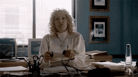 a woman is sitting at a desk in an office holding a magnifying glass .