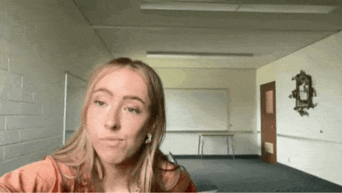 a young woman is sitting in an empty classroom with a white board on the wall .