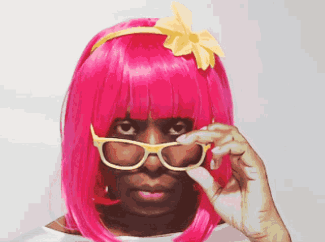 a woman wearing a pink wig and sunglasses looks over her glasses