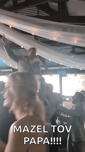 a group of people are dancing at a wedding reception and a man is holding a girl on his shoulders .