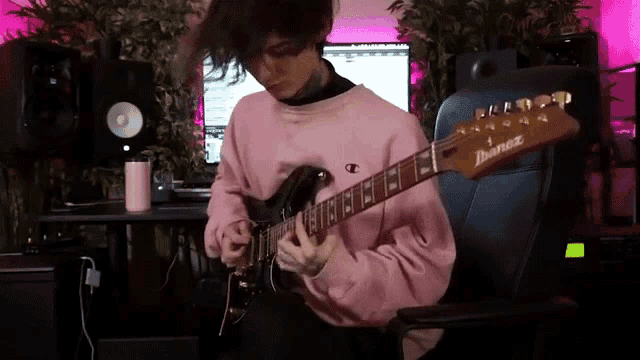 a man in a pink sweater is playing an ibanez electric guitar