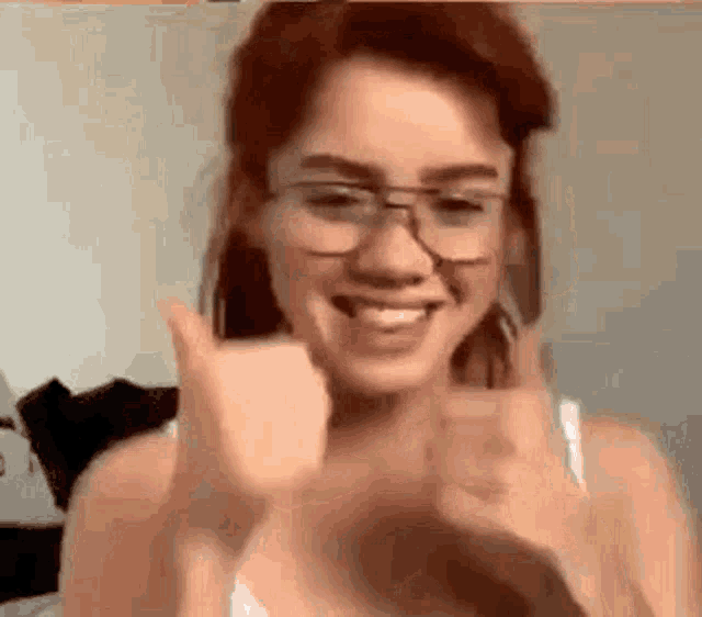 a woman wearing glasses is smiling and giving a thumbs up sign .