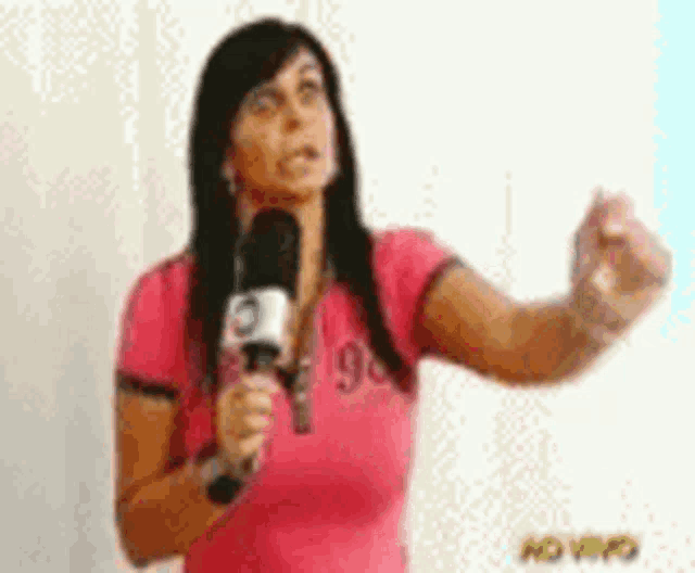 a woman in a pink shirt is holding a microphone in her hand