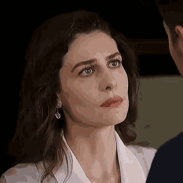 a woman in a white shirt and earrings is looking at a man in a blue shirt .