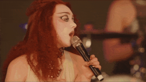 a woman with red hair singing into a microphone in front of a drum set