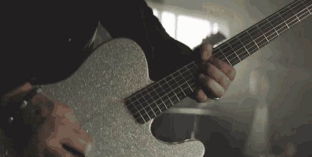 a man is playing a silver electric guitar in a room .