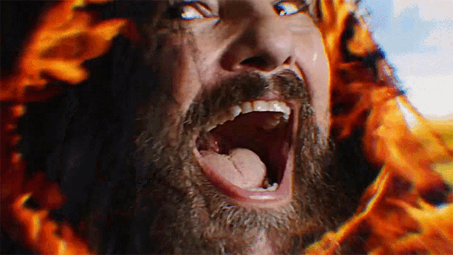 a man with a beard is screaming in front of a fire background