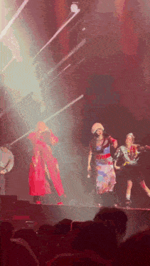 a woman in a red coat is standing on a stage with other people
