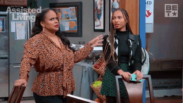 two women are standing next to each other in a kitchen talking .