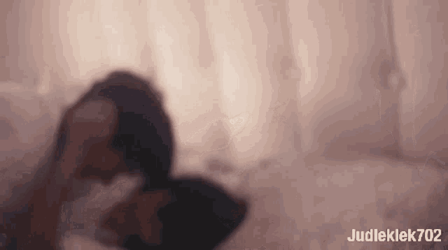 a blurry picture of a woman laying on a bed with judleklek702 written in the corner