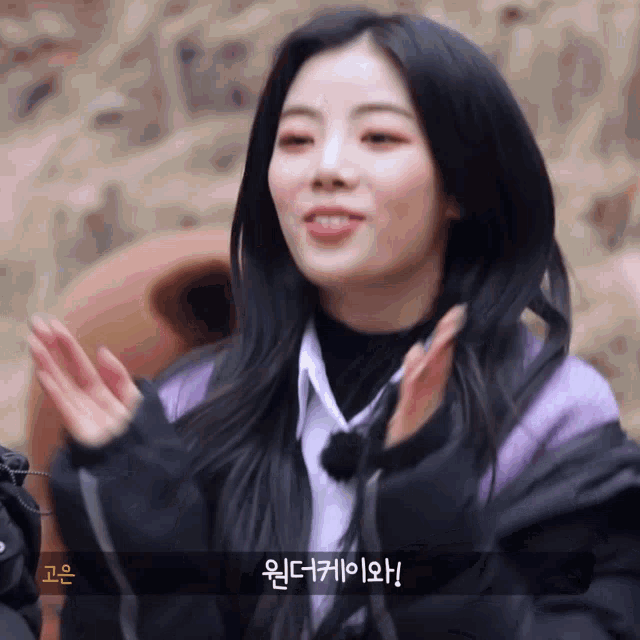 a girl in a purple jacket is clapping her hands in korean