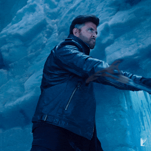 a man in a black leather jacket is standing in front of a blue wall